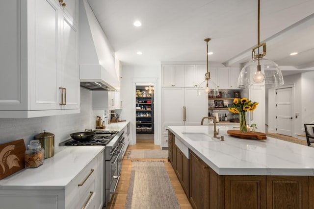 kitchen with premium range hood, sink, decorative light fixtures, high end stainless steel range, and white cabinets