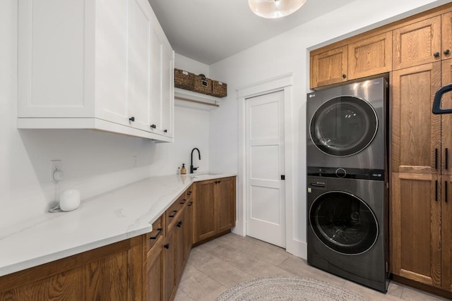 laundry area with stacked washer / drying machine, light tile patterned flooring, cabinets, and sink