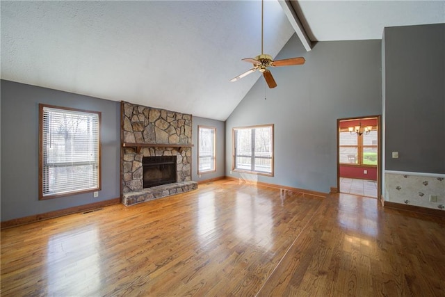 unfurnished living room featuring a stone fireplace, wood finished floors, ceiling fan with notable chandelier, and a healthy amount of sunlight