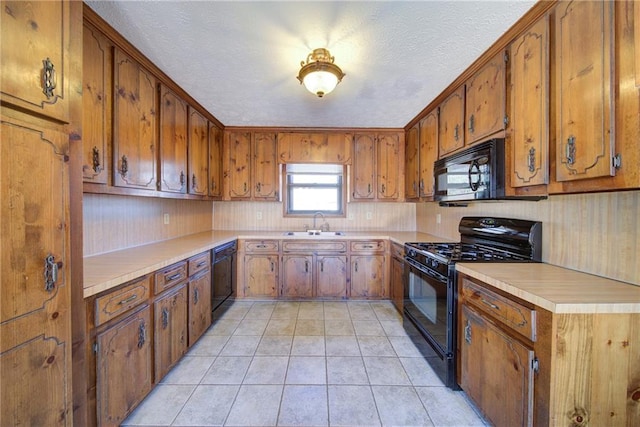 kitchen featuring light countertops, light tile patterned floors, brown cabinets, black appliances, and a sink