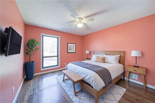 bedroom with visible vents, a textured ceiling, wood finished floors, baseboards, and ceiling fan