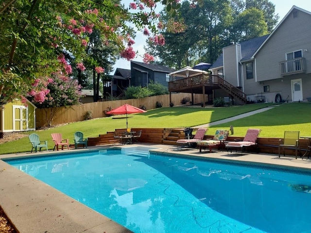 view of pool with an outbuilding, a fenced backyard, a storage unit, a deck, and a lawn