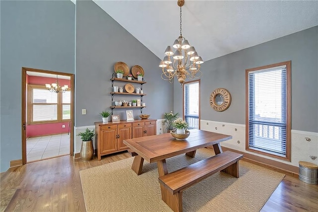 dining space featuring light wood finished floors, wainscoting, high vaulted ceiling, and an inviting chandelier