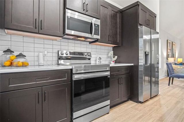 kitchen with dark brown cabinets, light hardwood / wood-style floors, decorative backsplash, and appliances with stainless steel finishes