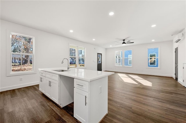 kitchen with ceiling fan, a wall mounted AC, a kitchen island with sink, sink, and white cabinets