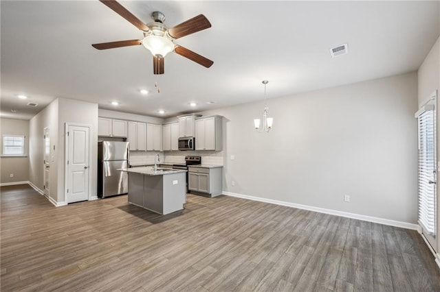 kitchen featuring appliances with stainless steel finishes, decorative light fixtures, an island with sink, gray cabinetry, and light stone counters