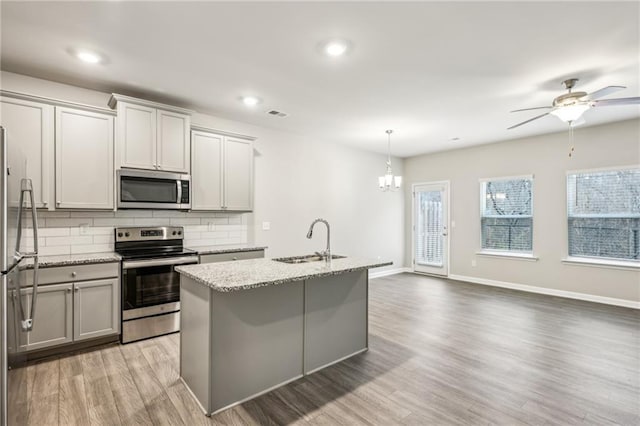 kitchen featuring sink, decorative light fixtures, appliances with stainless steel finishes, light stone countertops, and a kitchen island with sink