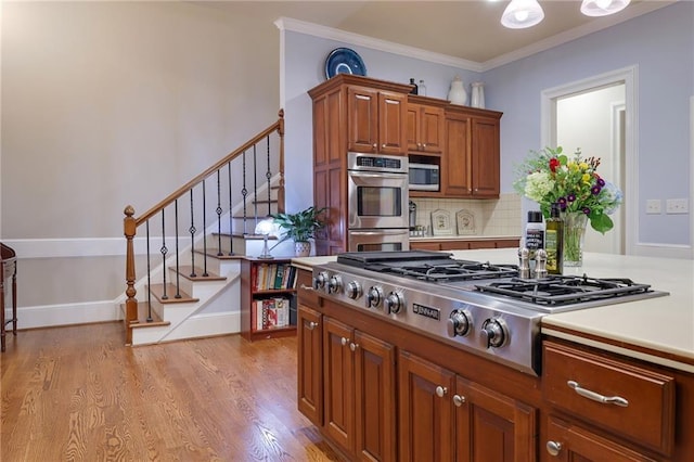 kitchen with tasteful backsplash, ornamental molding, appliances with stainless steel finishes, and light hardwood / wood-style flooring