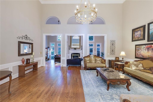 living room with a notable chandelier, light wood-type flooring, and a towering ceiling