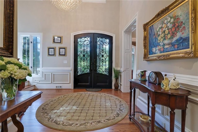 entrance foyer with a towering ceiling, french doors, a notable chandelier, and light wood-type flooring