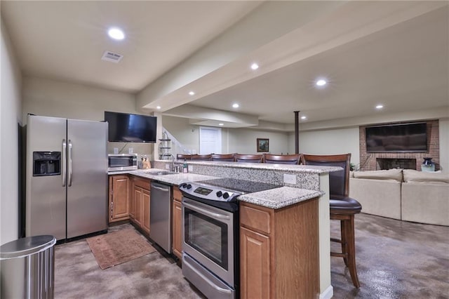 kitchen featuring light stone counters, a kitchen bar, stainless steel appliances, a fireplace, and sink