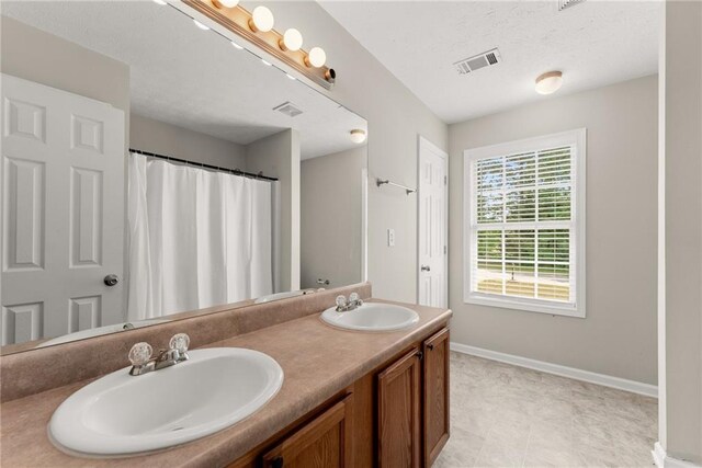 full bath with double vanity, baseboards, visible vents, and a sink