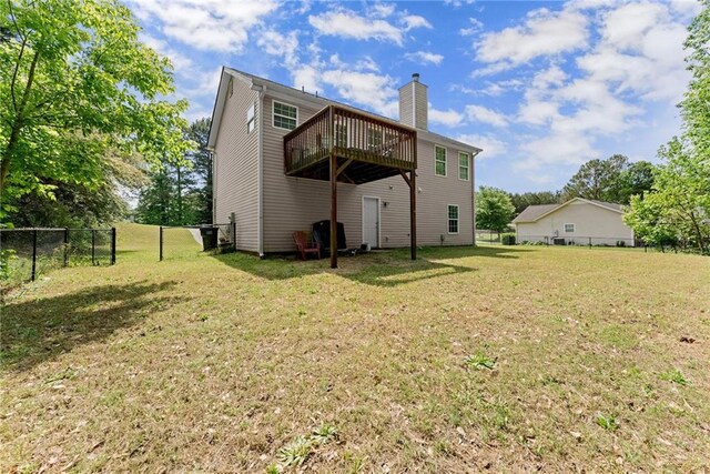 rear view of house with a lawn, a wooden deck, fence, and a chimney