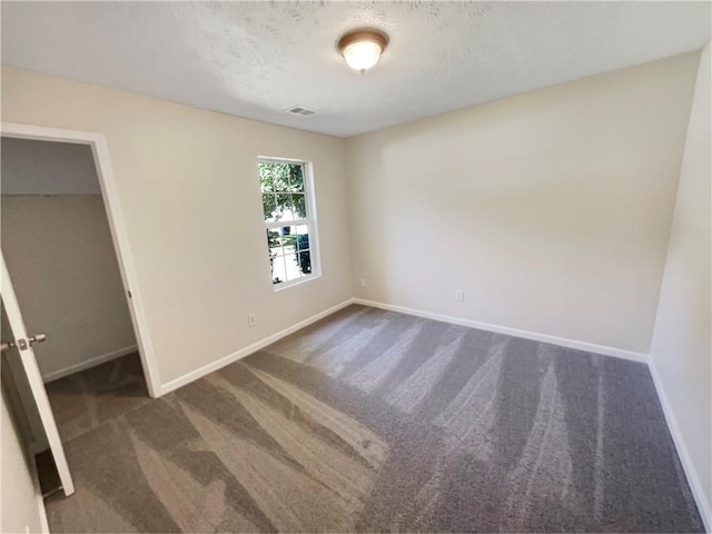 unfurnished bedroom featuring a spacious closet, dark carpet, and a textured ceiling