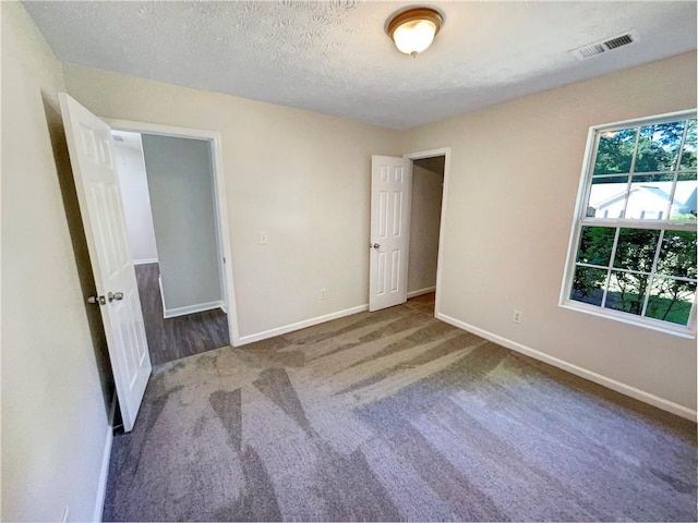 unfurnished bedroom featuring a textured ceiling and dark colored carpet