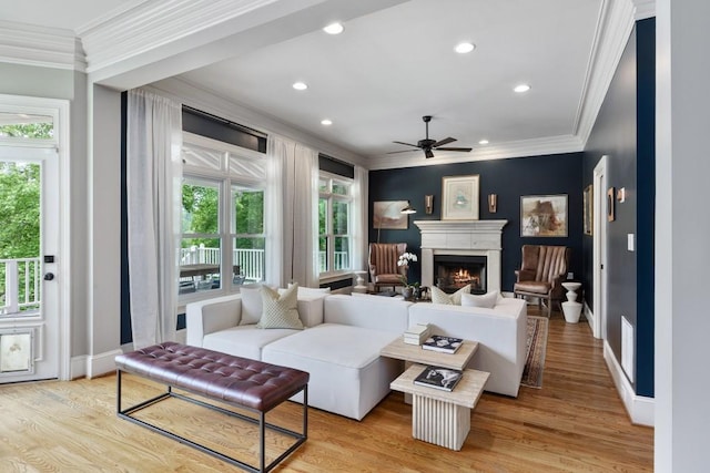 living area with ornamental molding, light wood finished floors, a ceiling fan, and a warm lit fireplace