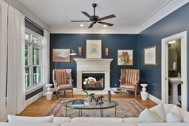 sitting room with baseboards, ceiling fan, a warm lit fireplace, and wood finished floors