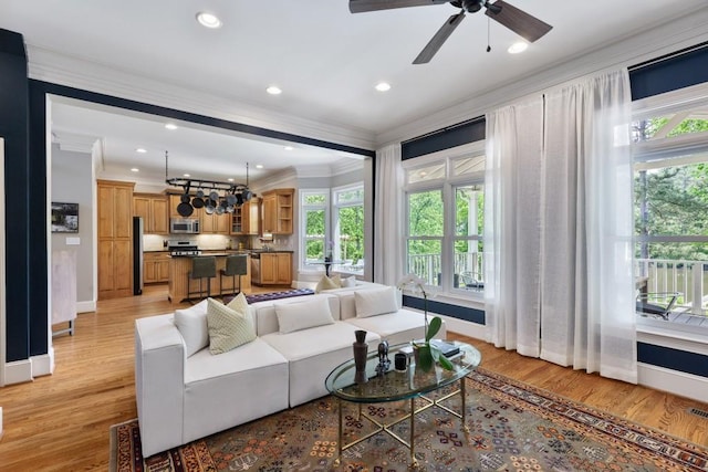 living area with baseboards, ceiling fan with notable chandelier, light wood-style floors, ornamental molding, and recessed lighting