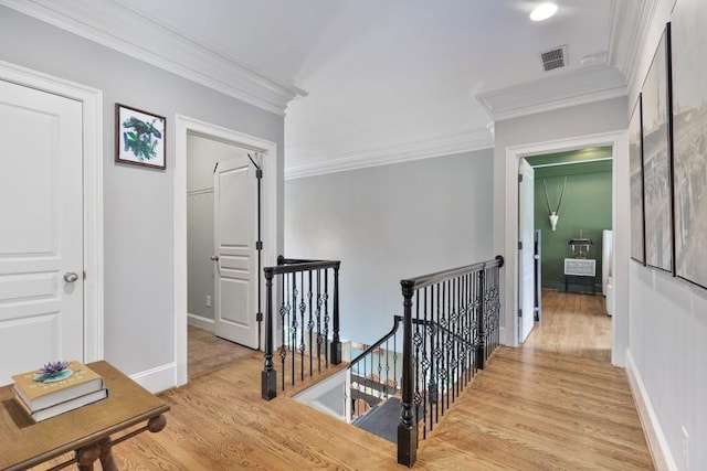 hallway with crown molding, visible vents, light wood-style flooring, and an upstairs landing