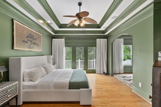 bedroom with ornamental molding, wood finished floors, access to outside, a tray ceiling, and arched walkways