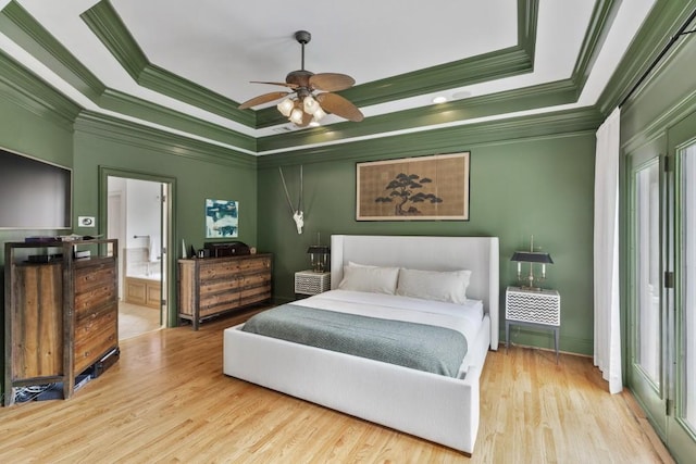 bedroom featuring crown molding, ceiling fan, wood finished floors, ensuite bathroom, and a tray ceiling