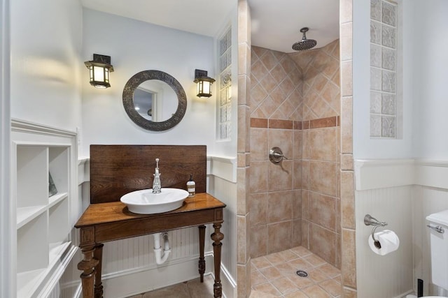 bathroom with a sink, tile patterned flooring, wainscoting, and a tile shower