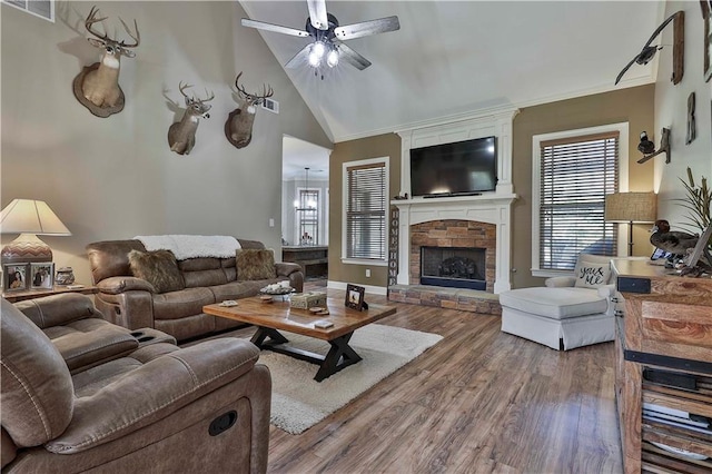 living room featuring ornamental molding, ceiling fan with notable chandelier, high vaulted ceiling, a fireplace, and hardwood / wood-style floors