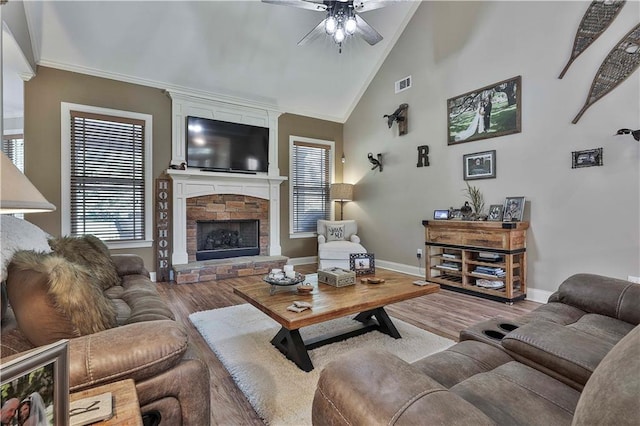 living room featuring high vaulted ceiling, crown molding, ceiling fan, a fireplace, and light hardwood / wood-style floors