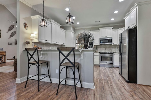 kitchen with appliances with stainless steel finishes, pendant lighting, a breakfast bar, white cabinets, and light wood-type flooring