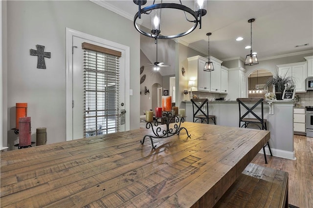 dining room with ornamental molding, ceiling fan with notable chandelier, and dark wood-type flooring