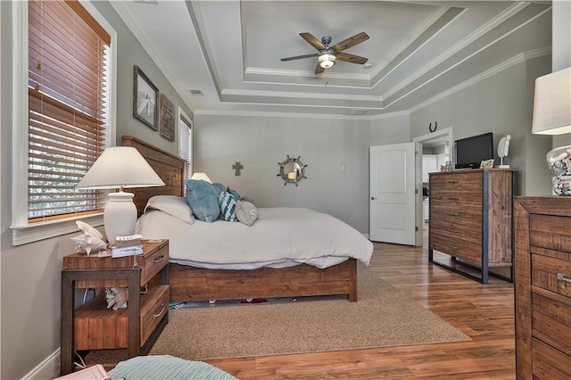 bedroom featuring ceiling fan, wood-type flooring, crown molding, and a tray ceiling