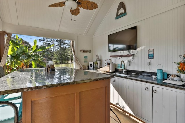 kitchen featuring vaulted ceiling, ceiling fan, dark stone countertops, and sink