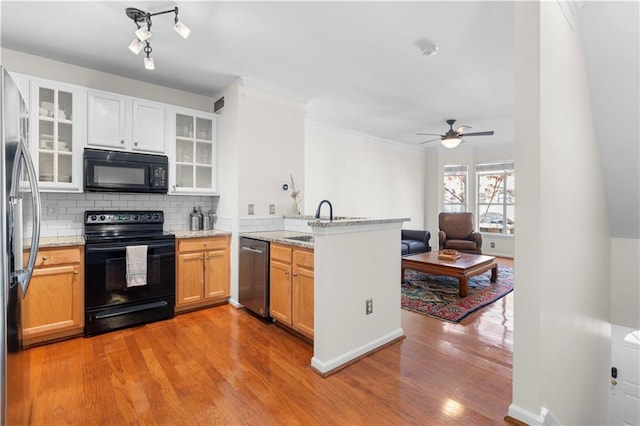 kitchen featuring tasteful backsplash, a peninsula, light wood-style floors, black appliances, and a sink