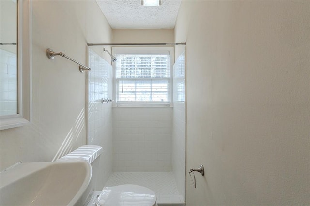 bathroom with tiled shower, a textured ceiling, and toilet