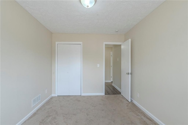 unfurnished bedroom featuring light colored carpet, a closet, and a textured ceiling