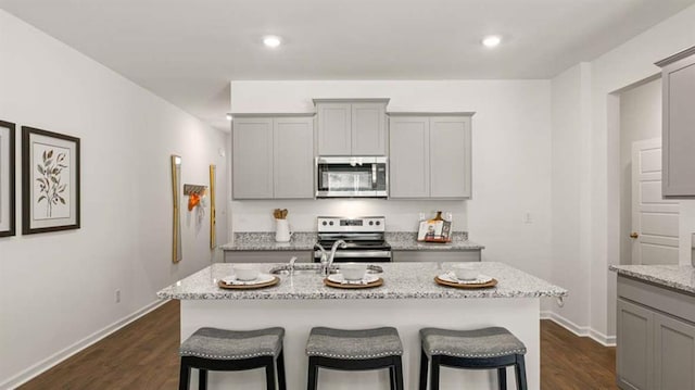 kitchen featuring dark wood finished floors, light stone counters, gray cabinets, and appliances with stainless steel finishes