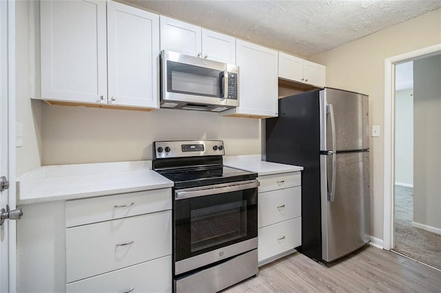 kitchen featuring white cabinets, a textured ceiling, stainless steel appliances, and light hardwood / wood-style floors