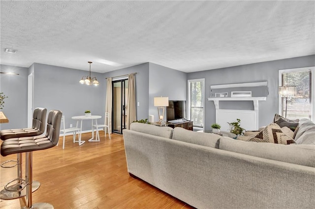 living area with a textured ceiling, baseboards, visible vents, light wood-style floors, and a notable chandelier