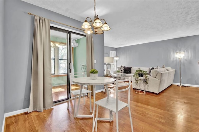 dining space with baseboards, a notable chandelier, a textured ceiling, and light wood-style flooring