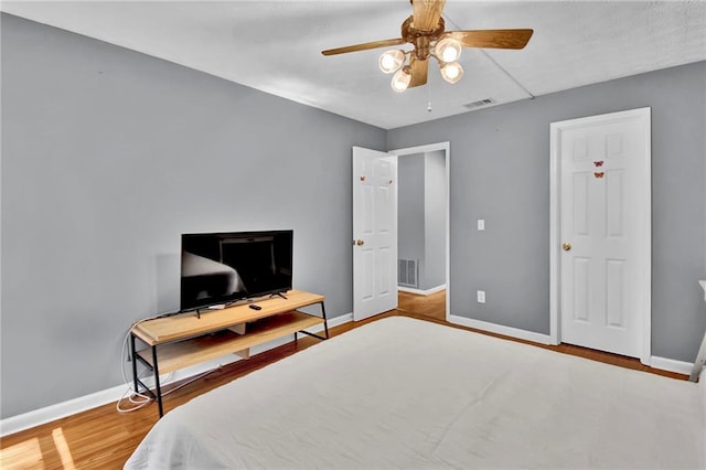 bedroom featuring baseboards, a ceiling fan, wood finished floors, and visible vents