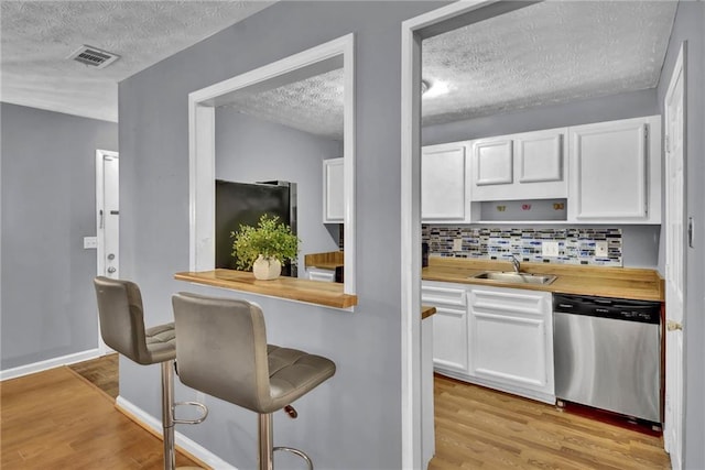 kitchen with white cabinets, a textured ceiling, stainless steel dishwasher, and a sink