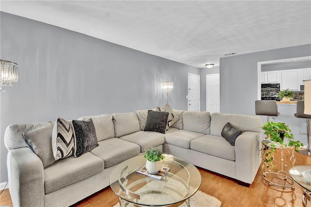 living area featuring visible vents, light wood-style floors, and a notable chandelier