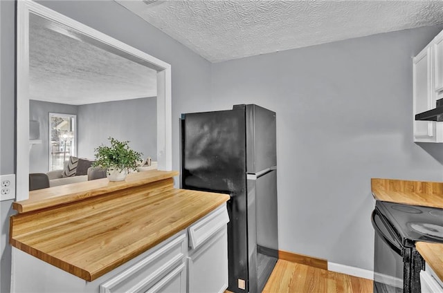 kitchen featuring light wood finished floors, wood counters, a textured ceiling, and black appliances