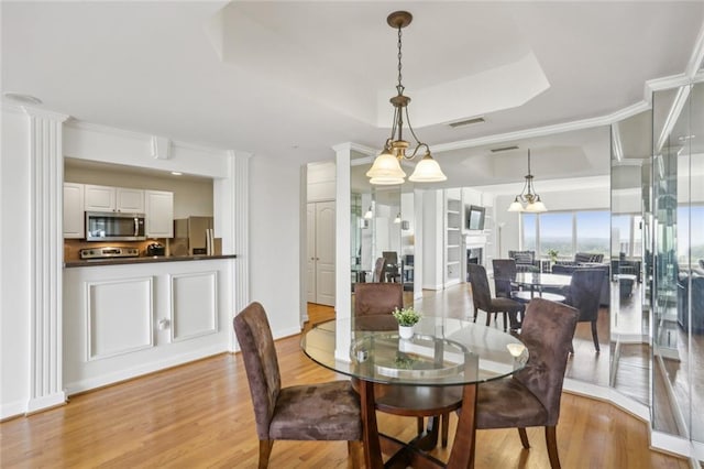 dining space with a raised ceiling, light wood-style flooring, visible vents, and decorative columns