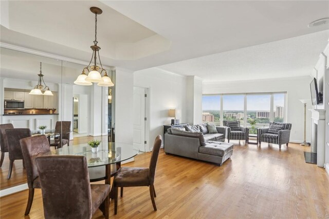 dining area with a tray ceiling, ornamental molding, light wood finished floors, and a fireplace