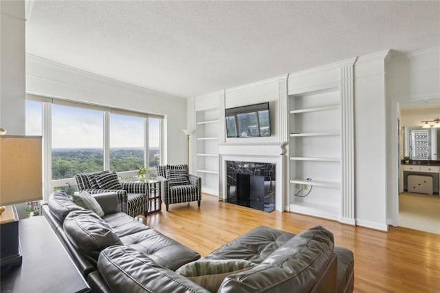 living area with a premium fireplace, a textured ceiling, built in features, crown molding, and wood finished floors
