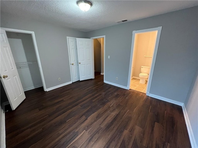 unfurnished bedroom featuring a textured ceiling, dark hardwood / wood-style flooring, and ensuite bathroom