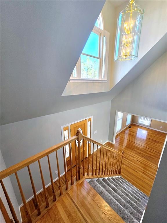 staircase with a towering ceiling, a chandelier, and wood finished floors