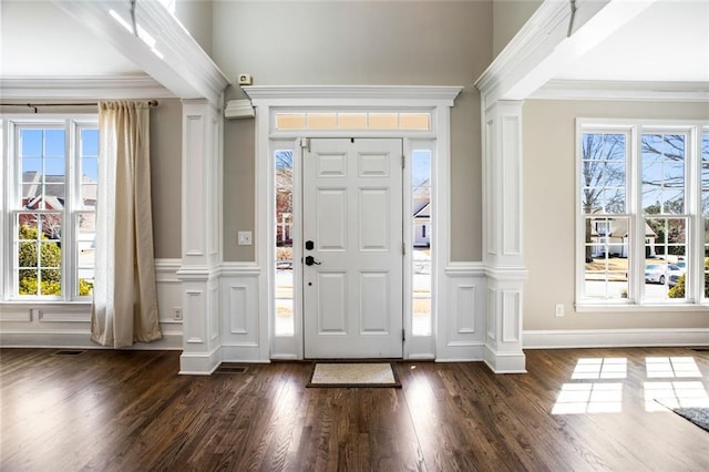 entryway featuring a wealth of natural light, crown molding, and decorative columns