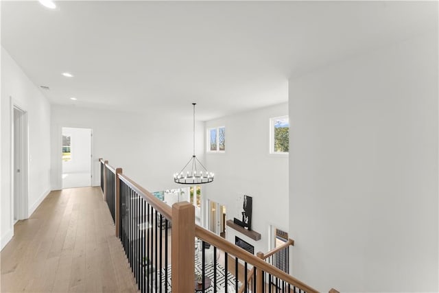 corridor with baseboards, light wood finished floors, recessed lighting, an upstairs landing, and a chandelier